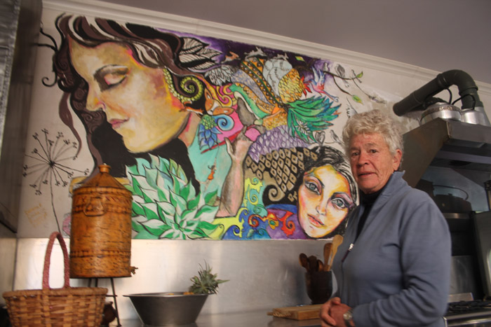 Me. Lourina Coetzee by die kombuismuur wat een van die deelnemers geverf het.